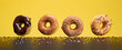 Four assorted donuts with different toppings hover over a yellow surface sprinkled with colorful candy pieces.