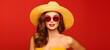 Summer studio portrait of beautiful brunette girl in red sunglasses and yellow swimsuit on red background with copy space