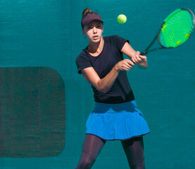 Wall Mural - A girl plays tennis on a court with a hard blue surface on a summer sunny da