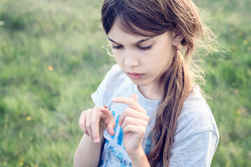 Wall Mural - Little girl on the background of a green field looking at a ladybug on her finger