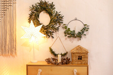 Wall Mural - Living room interior with wooden chest of drawers and wicker lamp on floor near white wall. Beautiful cozy home decor, lamp in the shape of a star and decorative wreaths of branches on white wall.	