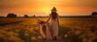 Back view of a woman in a field of flowers with her labrador dog at sunset, wearing a summer dress and hat. 