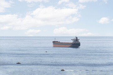 Empty cargo ship sailing along the coast of Alicante and surrounded by small boats.