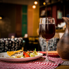 Wall Mural - Greek salad and glass of red wine on the oak table