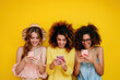 © wolfhound911 - Three beautiful young women looking at smartphones on a orange background