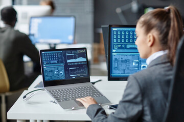 Over shoulder view of female IT security specialist using multiple computers with blue data on screen copy space