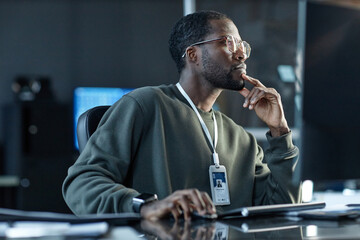 side view portrait of black young man wearing glasses and thinking in pro company office looking awa