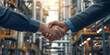 Businessmen shaking hands and collaborating on a business deal against the backdrop of an industrial factory.