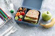 School lunch box with sandwich, vegetables, fruit and water on table, healthy eating concept.