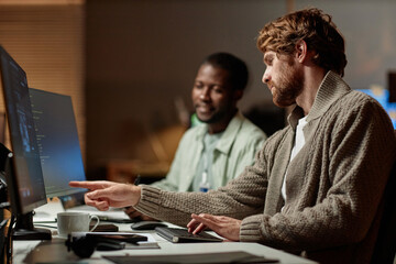 Side view portrait of bearded man pointing at computer screen and talking to colleague while reviewing data in office, copy space