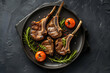 Perfectly grilled lamb chops served on plate on a black table. Tasty appetizing dish in restaurant food service. Top view