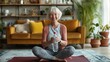 Cheerful elderly fitness enthusiast enjoying break after indoor workout, holding water bottle, smiling at camera while sitting on yoga mat in living room