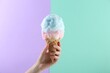 Woman holding waffle cone with cotton candy on color background, closeup