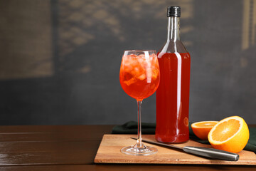 Aperol spritz cocktail and ice cubes in glass and bottle on wooden table, space for text