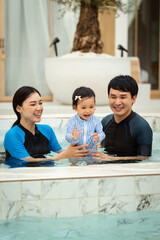 Wall Mural - happy family. father and mother with small daughter in swimming pool.