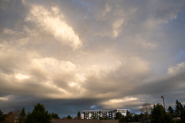 Wall Mural - Modern apartment building below a stormy winter sky with clouds highlighted by the setting sun
