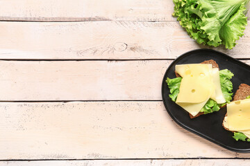 Canvas Print - Tasty sandwiches with cheese and lettuce in plate on light wooden background