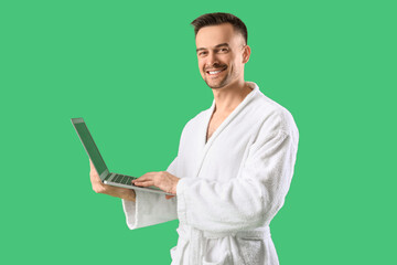 Canvas Print - Happy young man in bathrobe with laptop on green background