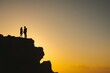 © primopiano - silhouettes of pair standing on cliff, sunrise in background