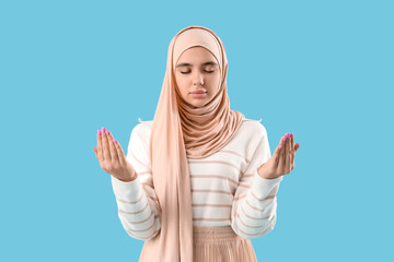 Canvas Print - Young Muslim woman in hijab praying on blue background