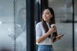 © Wasana - A cheerful young businesswoman engaging in a phone conversation while holding a coffee cup, inside a bright modern office space..