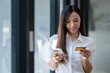 © Wasana - Smiling young woman using smartphone and holding credit card, potentially making an online purchase..