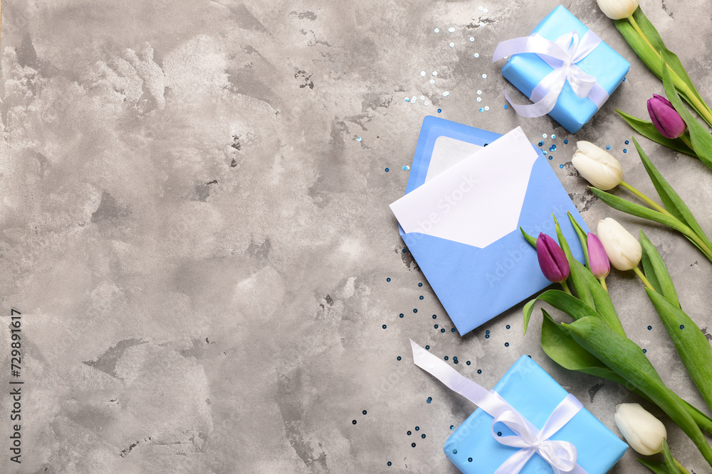 Envelope with blank card, gift boxes and tulip flowers on grey grunge background. International Women's Day celebration