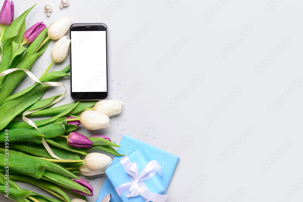 Composition with modern mobile phone, beautiful tulip flowers and gift box on grey background