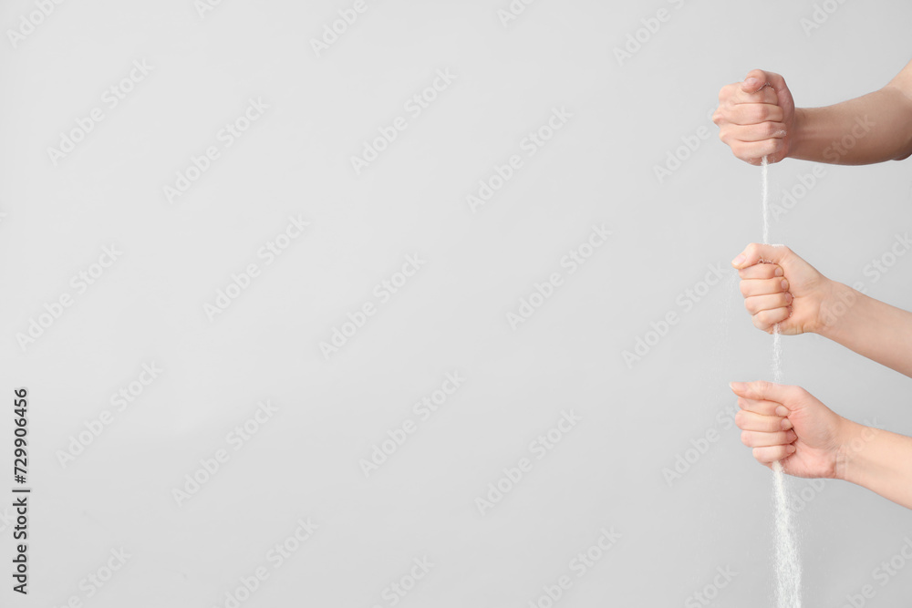Many hands with pouring sand on grey background. Time concept