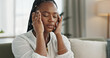 © Coetzee/peopleimages.com - Headache, stress and young black woman in the living room of her modern apartment on weekend. Burnout, mental health and sick African female person with migraine for illness in lounge at home.