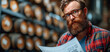 Portrait of a handsome red-bearded winemaker in a red plaid shirt and glasses doing a check on his business