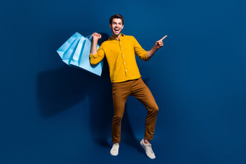 Sticker - Full length photo of nice young male shopping bags point empty space dressed stylish yellow garment isolated on dark blue color background