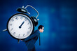 © Creativa Images - Side view of young handsome man carrying huge alarm clock on his back