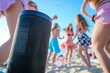 closeup of a black bluetooth speaker with teens dancing at a beach party