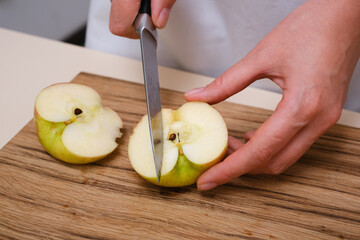 female cook slices an apple on a wooden board in her kitchen