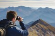 man at peak, looking at distant mountains through binoculars