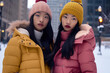 © Antonio - Winter Fashion - Two Young Women wearing matching coats and knitted beanies in the snow near the City Skyline
