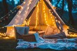 tent aglow with string lights, picnic basket and blankets outside