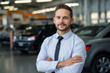Fototapeta Do przedpokoju - Portrait of car salesman standing in front of new vehicles in car dealership. 