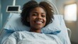Portrait of a young black woman with a bright smile, lying in a hospital bed, with medical equipment in the background.