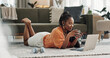 © Coetzee/peopleimages.com - Laptop, coffee and woman on the floor in living room of modern apartment reading information. Technology, relax and young African female student study and drink latte on computer in lounge at home.