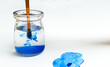 A brush with blue paint is washed in a glass jar with water, blue cloud. Paint dripping into water, white sheet of paper, blue cloud painted with watercolors on canvas, space for copy