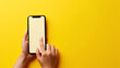 A hand is holding a smartphone with a blank screen against a vibrant yellow background, tapping the screen with one finger.