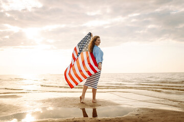 Happy woman holding United States of America flag and running  on the beach at sunset. Patriotic holiday. USA celebrate 4th of July. Independence Day concept