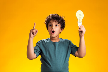 Surprised child boy holding paper bulb and holding finger up. Success, motivation, winner, genius, idea concept