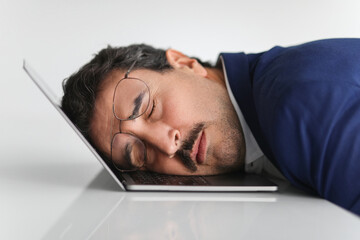 Wall Mural - An overworked businessman in a blue suit takes a nap on his laptop keyboard in an office