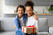 © Prostock-studio - Joyful black mother and son with gift box on sofa