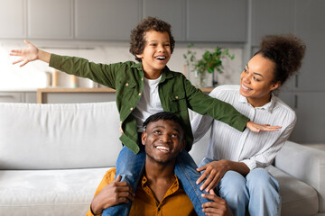 Wall Mural - Black boy plays airplane with parents' support at home