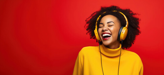 Happy afro american woman with curly hair and bright yellow jumper listening to the music and laughing, red background, banner