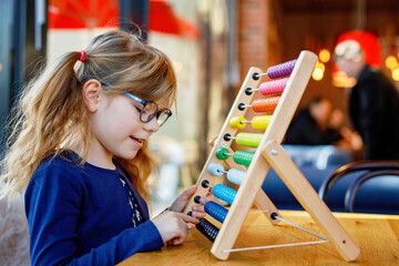 Wall Mural - Little preschool girl playing with educational wooden rainbow toy counter abacus. Healthy happy child with glasses learning to count and colors, indoors on sunny day.